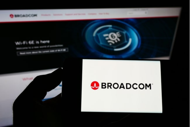 Person håller mobil med broadcoms logga på skärmen framför skärm med företagets webbsida öppen.