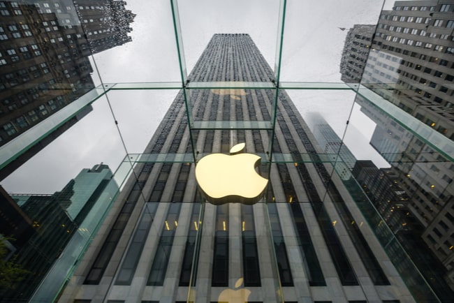 Apples logga i guld mot svartvit husfasad.
